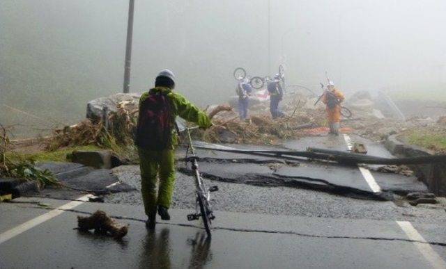 自転車を担いで崩壊した道路を進む様子の写真