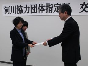 髙橋治水課長から指定証を受け取る小山内会長（左）