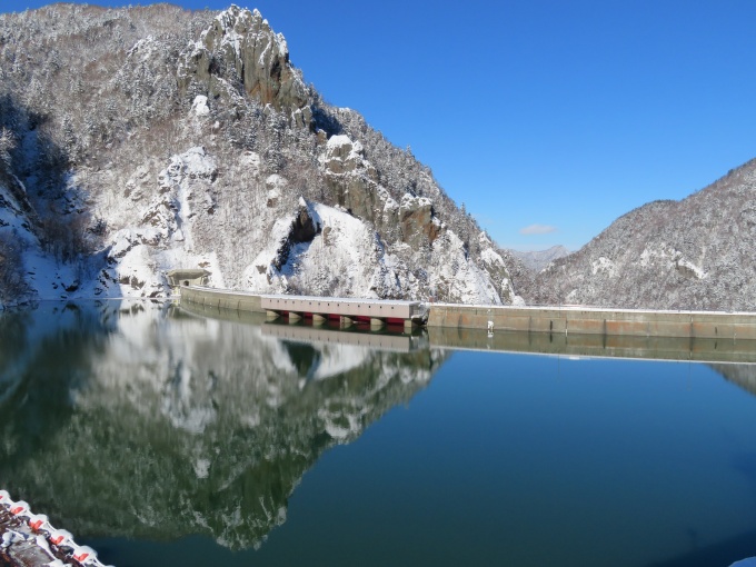 管理支所から眺めたダム湖に山が映っている写真