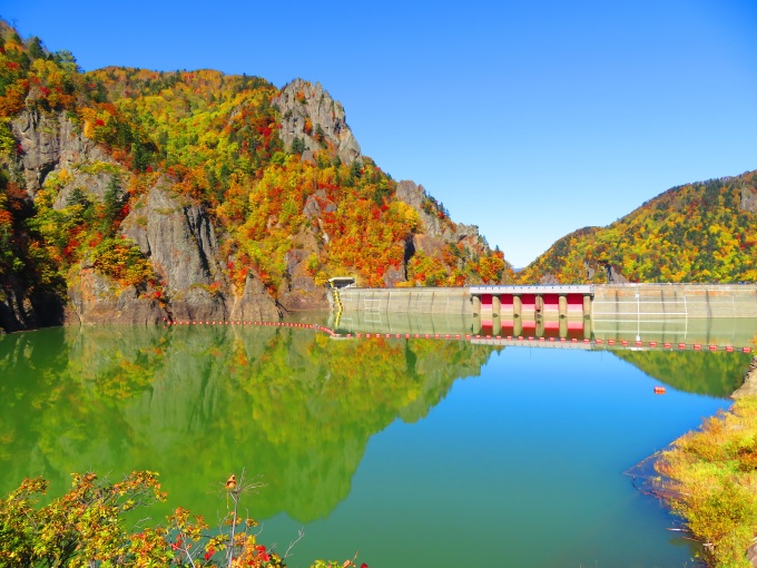 鏡のようなダム湖の水面に映る紅葉の写真